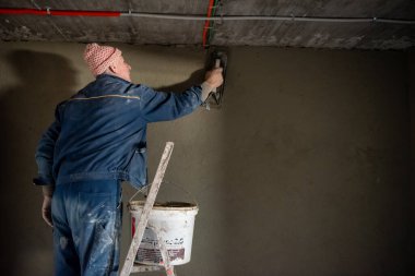 İnşaat işçisi inşaat alanındaki duvarı beton sıva işçisiyle kaplıyor.