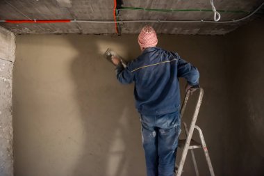 İnşaat işçisi inşaat alanındaki duvarı beton sıva işçisiyle kaplıyor.