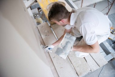 Genç profesyonel inşaat işçisi alçıtaşı duvarlara sıva yapıyor. Yeni, büyük, modern iki katlı apartmanın içinde.