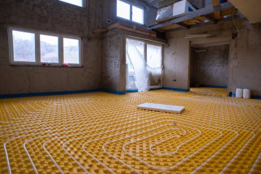 İki katlı yeni bir apartmanın şantiyesinde beyaz polietilen boruları olan sarı yeraltı ısıtma tesisatı.