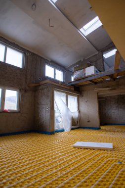 İki katlı yeni bir apartmanın şantiyesinde beyaz polietilen boruları olan sarı yeraltı ısıtma tesisatı.