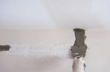 Genç profesyonel inşaat işçisi alçıtaşı duvarlara sıva yapıyor. Yeni, büyük, modern iki katlı apartmanın içinde.