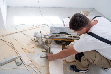 Profesyonel işçi, kurulum sırasında elektrikli testere ile tahta kesiyor. Tamamlanmamış bir dairede yeni bir ahşap döşeme.