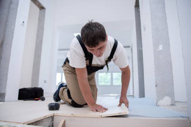professional carpenter installing new laminated wooden floor in a unfinished apartment clipart