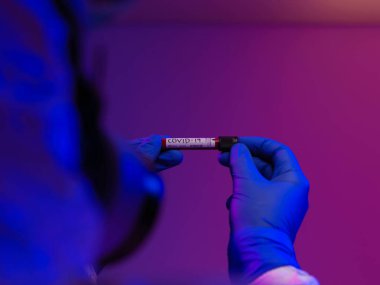 Coronavirus, doktorun elinde kovid 19 virüslü kan örneği tüpü var. Biyolojik tehlike salgını var Koruyucu maske, kostüm ve ışıltı.