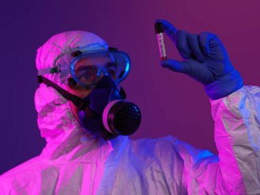 Coronavirus, doktorun elinde kovid 19 virüslü kan örneği tüpü var. Biyolojik tehlike salgını var Koruyucu maske, kostüm ve ışıltı.