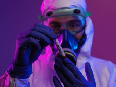 Coronavirus, doktorun elinde kovid 19 virüslü kan örneği tüpü var. Biyolojik tehlike salgını var Koruyucu maske, kostüm ve ışıltı.