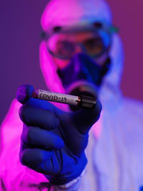 Coronavirus, doktorun elinde kovid 19 virüslü kan örneği tüpü var. Biyolojik tehlike salgını var Koruyucu maske, kostüm ve ışıltı.