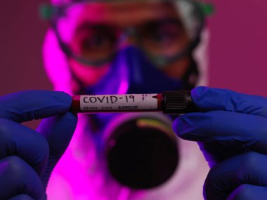 Coronavirus, doktorun elinde kovid 19 virüslü kan örneği tüpü var. Biyolojik tehlike salgını var Koruyucu maske, kostüm ve ışıltı.