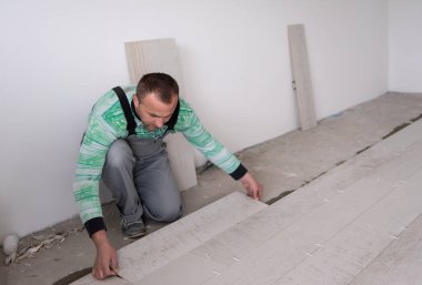 Seramik ahşap efekt fayanslarını döşeyen yetenekli bir işçi. İşçi, yeni apartmanın inşaat alanında döşeme kaplaması yapıyor.