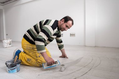 Grouting ceramic tiles. Tilers filling the space between ceramic wood effect tiles using a rubber trowel on the floor in new modern apartment clipart