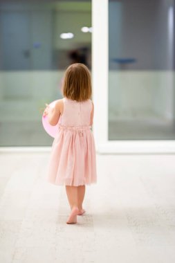 Pembe elbiseli mutlu küçük kız güzel bir akşamda evdeki pencerenin yanında balonlarla oynarken eğleniyor.