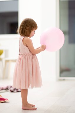 Pembe elbiseli mutlu küçük kız güzel bir akşamda evdeki pencerenin yanında balonlarla oynarken eğleniyor.