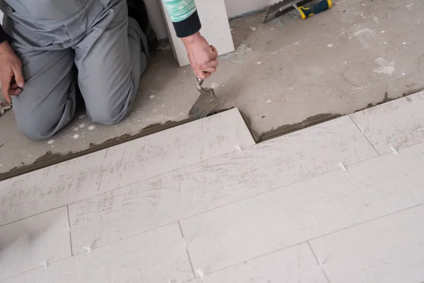 在新公寓的建筑工地上安装陶瓷砖的熟练工人在地板上制造层压板地板 — 图库照片