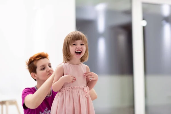 家庭で楽しい夜を過ごしてる若いお母さんかわいい娘を助けながらピンクのドレスを着て家で踊る — ストック写真