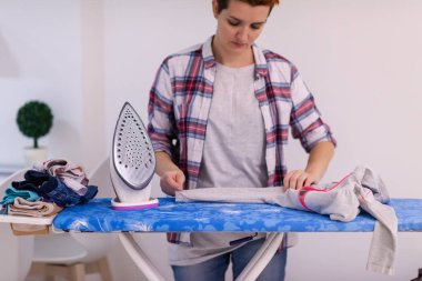 Güzel, genç, kızıl saçlı ev hanımı. Keyfi yerinde. Evde beyaz bir duvarın önündeki ütü masasında giysilerini ütülüyor.