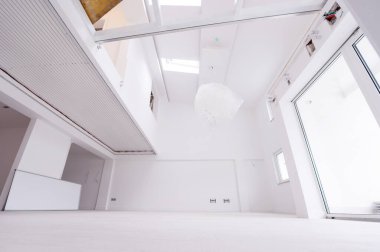 Boş, şık, modern, iki katlı, beyaz duvarları ve ortasındaki büyük, yuvarlak avizesi olan bir apartman dairesi.