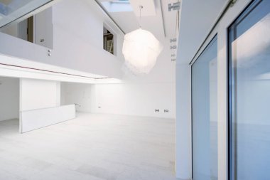 Boş, şık, modern, iki katlı, beyaz duvarları ve ortasındaki büyük, yuvarlak avizesi olan bir apartman dairesi.