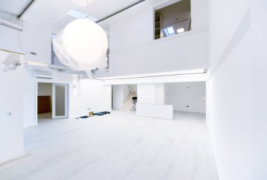 Boş, şık, modern, iki katlı, beyaz duvarları ve ortasındaki büyük, yuvarlak avizesi olan bir apartman dairesi.