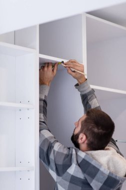 Yeni moda modern mutfak mobilyalarının montajı sırasında tedbirleri yazan genç profesyonel işçi