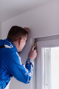 Genç profesyonel inşaat işçisi alçıtaşı duvarlara sıva yapıyor. Yeni, büyük, modern iki katlı apartmanın içinde.