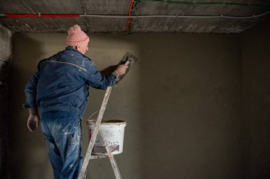 İnşaat işçisi inşaat alanındaki duvarı beton sıva işçisiyle kaplıyor.