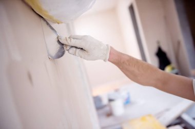 Genç profesyonel inşaat işçisi alçıtaşı duvarlara sıva yapıyor. Yeni, büyük, modern iki katlı apartmanın içinde.