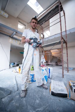 Profesyonel erkek müteahhit, henüz tamamlanmamış dairede elektrikli mikser kullanarak alçıyı kovaya karıştırıyor.