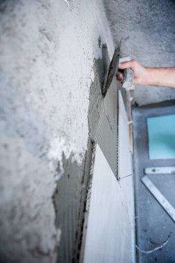 Tecrübeli inşaat işçisi iç beton duvarlara büyük seramik fayanslar yerleştiriyor.