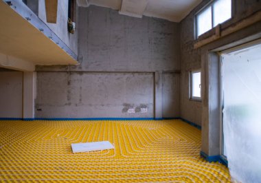 İki katlı yeni bir apartmanın şantiyesinde beyaz polietilen boruları olan sarı yeraltı ısıtma tesisatı.