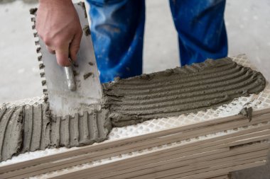 Seramik ahşap efekt fayanslarını döşeyen yetenekli bir işçi. İşçi, yeni apartmanın inşaat alanında döşeme kaplaması yapıyor.