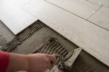 Seramik ahşap efekt fayanslarını döşeyen yetenekli bir işçi. İşçi, yeni apartmanın inşaat alanında döşeme kaplaması yapıyor.