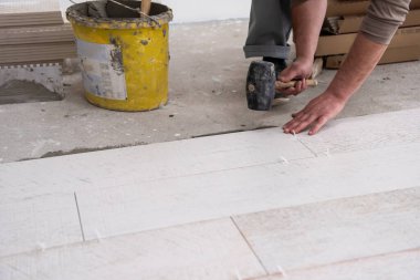 Seramik ahşap efekt fayanslarını döşeyen yetenekli bir işçi. İşçi, yeni apartmanın inşaat alanında döşeme kaplaması yapıyor.