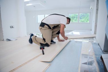 Profesyonel marangoz tamamlanmamış bir daireye yeni ahşap döşeme kuruyor.