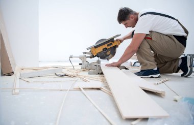 Profesyonel işçi, kurulum sırasında elektrikli testere ile tahta kesiyor. Tamamlanmamış bir dairede yeni bir ahşap döşeme.