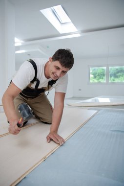 Profesyonel marangoz, tamamlanmamış bir daireye yeni kaplamalı ahşap döşeme yaparken plastik çekiç kullanıyor.