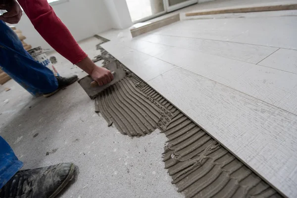 在新公寓的建筑工地上安装陶瓷砖的熟练工人在地板上制造层压板地板 — 图库照片