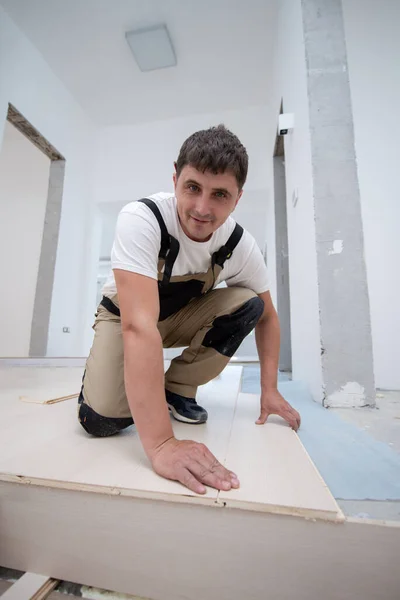 在未完工的公寓中安装新的层压木地板的专业木匠 — 图库照片