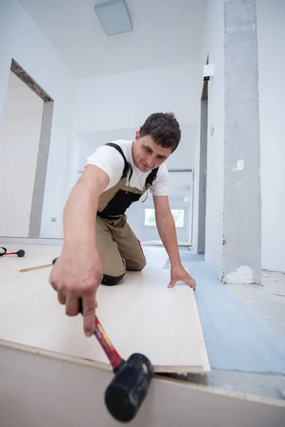 在未完工的公寓中安装新的层压板地板时使用橡胶锤的专业木匠 — 图库照片