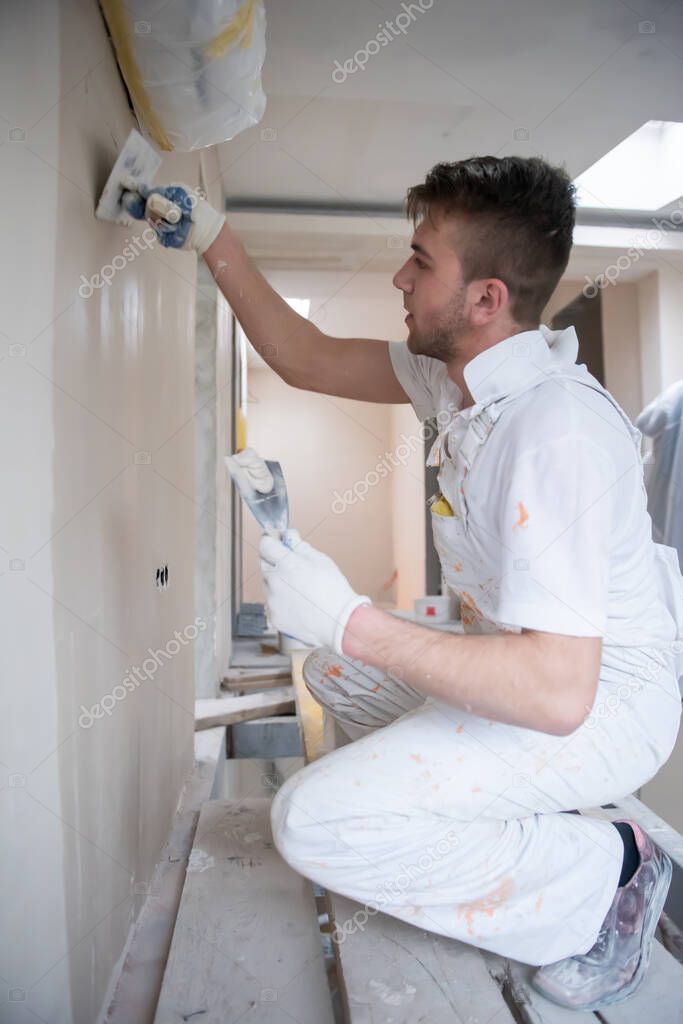 young professional construction worker plastering on gypsum walls inside the new big modern two levels apartment