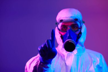 Coronavirus covid-19 salgını. Küresel sağlık salgını uyarısı ve mavi ve pembe neon ışıklı arka plandaki tehlike nedeniyle koruyucu biyolojik kıyafet ve maske giyen doktor..