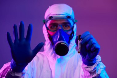 Coronavirus, doktorun elinde kovid 19 virüsü var. Kan örneği test tüpü. Biyolojik tehlike salgını maskesi, giysisi ve parlak ışık arkaplanı var.