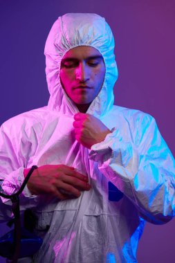 Coronavirus covid-19 salgını. Küresel sağlık salgını uyarısı ve mavi ve pembe neon ışıklı arka plandaki tehlike nedeniyle koruyucu biyolojik kıyafet ve maske giyen doktor..