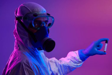 Coronavirus, doktorun elinde kovid 19 virüsü var. Kan örneği test tüpü. Biyolojik tehlike salgını maskesi, giysisi ve parlak ışık arkaplanı var.