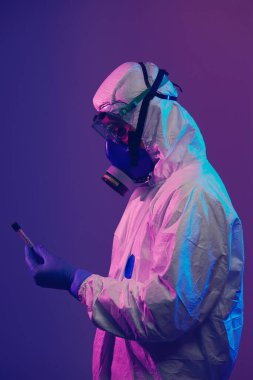 Coronavirus, doktorun elinde kovid 19 virüsü var. Kan örneği test tüpü. Biyolojik tehlike salgını maskesi, giysisi ve parlak ışık arkaplanı var.