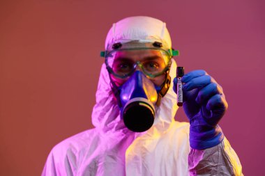 Coronavirus, doktorun elinde kovid 19 virüsü var. Kan örneği test tüpü. Biyolojik tehlike salgını maskesi, giysisi ve parlak ışık arkaplanı var.