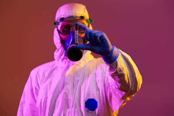 コロナウイルス 医師は正のCovid 19ウイルス血液サンプル検査管を保持します バイオハザードの流行を身に着けている保護マスク スーツ ネオンライトの背景を育てる — ストック写真