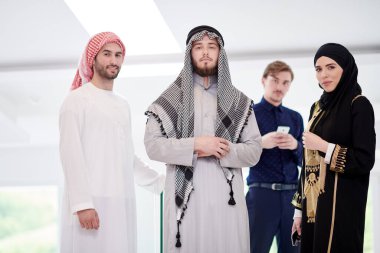 Modern İslami moda teknolojisini ve Ramazan Kareem kavramını temsil eden modern aydınlık evde akıllı telefon kullanan üç Arap erkeğiyle şık tesettürlü genç Müslüman kadınların grup portresi