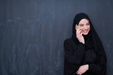 Genç, modern Müslüman iş kadını siyah karatahtanın önünde tesettürlü kıyafetler giyiyor.