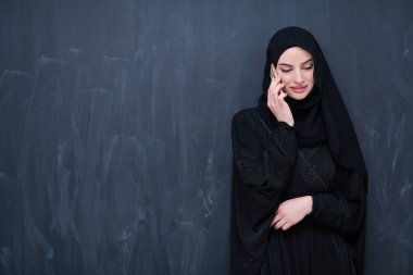 Genç, modern Müslüman iş kadını siyah karatahtanın önünde tesettürlü kıyafetler giyiyor.